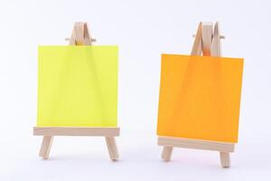 Two Wooden Easels Miniature with Blank Colored Square Canvas or Memo Paper - Mockup. Mini Wooden Stand with Clean Artboard on White Background, Copy Space photo