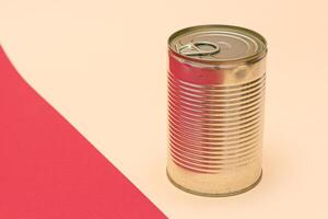 Unopened Tin Can with Blank Edge on Split Red and Beige Background. Canned Food. Aluminum Can for Safe and Long Term Storage of Food. Steel Sealed Food Storage Container photo