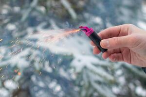 Burning Firecracker in a Hand. Guy Holding a Petard Outdoors in Winter at Daytime. Loud and Dangerous New Year's Entertainment. Hooliganism with Pyrotechnics. Noise of Firecrackers in Public Places photo