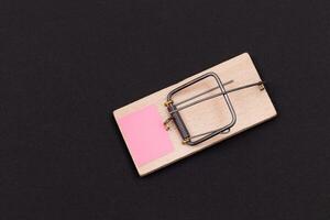 Blank Pink Sheet of Paper in Wooden Mousetrap - Template. Small Memo Paper in Mouse Trap on Black Background photo