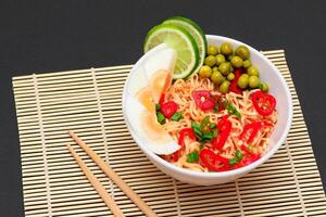 Beautiful Noodle Dish with Green Pea, Eggs, Red Hot Pepper, Greens and Lime with Chopsticks on Sushi Mat. Instant Noodles photo