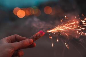 Young Man Lighting Up Firecracker in his Hand Outdoors in Evening. Guy Getting Ready for New Year Fun with Fireworks or Pyrotechnic Products - CloseUp Shot photo