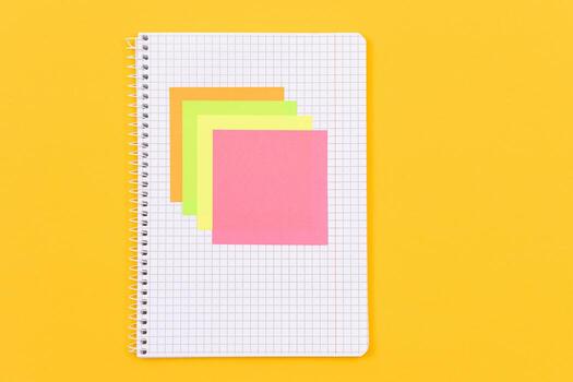 A Notepad with Sticky Notes Lying on Yellow Table - Blank Template. Top View, Flat Lay photo