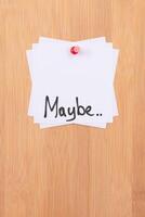 MAYBE.. - White Sticky Notes with Written Word MAYBE, Pinned to the Wooden Message Board. To Do List Reminder in the Office. Memo Note at Work photo
