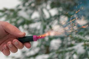 Burning Firecracker in a Hand. Guy Holding a Petard Outdoors in Winter at Daytime. Loud and Dangerous New Year's Entertainment. Hooliganism with Pyrotechnics. Noise of Firecrackers in Public Places photo