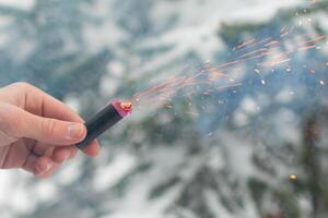 Burning Firecracker in a Hand. Guy Holding a Petard Outdoors in Winter at Daytime. Loud and Dangerous New Year's Entertainment. Hooliganism with Pyrotechnics. Noise of Firecrackers in Public Places photo