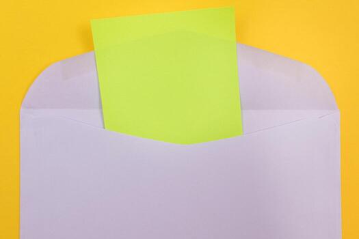 Violet Envelope with Blank Green Sheet of Paper Inside, Lying on Yellow Background - Mock Up with Copy Space. Receiving Mail or Notice, Sending Postcard - Top View, Flat Lay photo