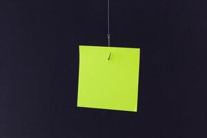 Mockup of a Blank Green Memo Paper with Copy Space Hanging on a Fishing Hook Against the Black Background. Reminder or To Do List. Sticky Note Template photo