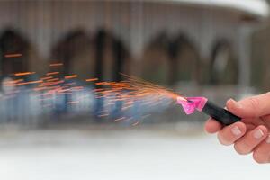 Burning Firecracker in a Hand. Guy Holding a Petard Outdoors in Winter at Daytime. Loud and Dangerous New Year's Entertainment. Hooliganism with Pyrotechnics. Noise of Firecrackers in Public Places photo