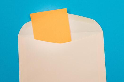 Beige Envelope with Blank Orange Sheet of Paper Inside, Lying on Blue Background - Mock Up with Copy Space. Receiving Mail or Notice, Sending Postcard - Top View, Flat Lay photo
