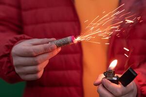 Man in Red Jacked Lighting Up Firecracker in his Hand Using Gasoline Lighter. Guy Getting Ready for New Year Fun with Fireworks or Pyrotechnic Products photo