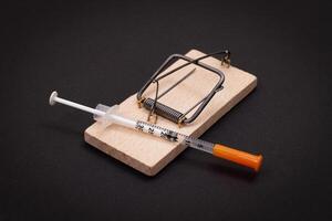 Drug Addict, Heroin Hazard or Dose Trap Concept - Disposable Insulin Syringe with Drug Dose Inside Lying in Wooden Mousetrap on Black Background photo