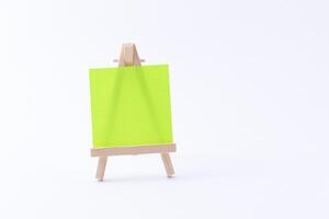 Wooden Easel Miniature with Blank Colored Square Canvas or Memo Paper - Mockup. Mini Wooden Stand with Clean Artboard on White Background, Copy Space photo