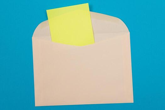 Beige Envelope with Blank Yellow Sheet of Paper Inside, Lying on Blue Background - Mock Up with Copy Space. Receiving Mail or Notice, Sending Postcard - Top View, Flat Lay photo