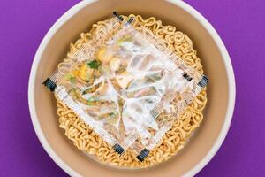 Opened Package with Uncooked Instant Noodles on Violet Background. Raw Pasta. Dry Asian Fast Food. Quick Lunch photo