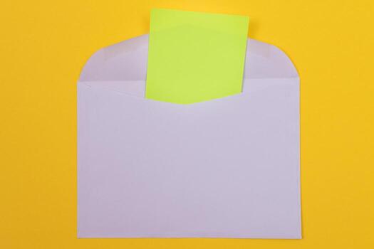Violet Envelope with Blank Green Sheet of Paper Inside, Lying on Yellow Background - Mock Up with Copy Space. Receiving Mail or Notice, Sending Postcard - Top View, Flat Lay photo