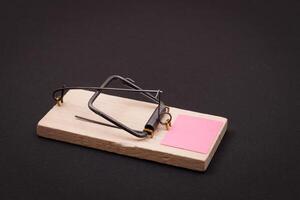 Blank Pink Sheet of Paper in Wooden Mousetrap - Template. Small Memo Paper in Mouse Trap on Black Background photo