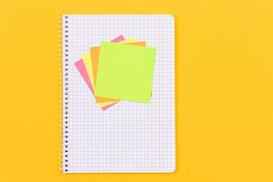 A Notepad with Sticky Notes Lying on Yellow Table - Blank Template. Top View, Flat Lay photo