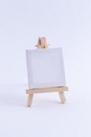 Wooden Easel Miniature with Blank White Square Canvas for Artists and Painters - Mockup. Mini Wooden Stand with Clean Artboard on White Background, Copy Space photo