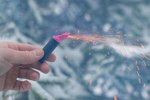 Burning Firecracker in a Hand. Guy Holding a Petard Outdoors in Winter at Daytime. Loud and Dangerous New Year's Entertainment. Hooliganism with Pyrotechnics. Noise of Firecrackers in Public Places photo