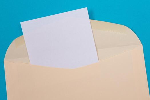 Beige Envelope with Blank White Sheet of Paper Inside, Lying on Blue Background - Mock Up with Copy Space. Receiving Mail or Notice, Sending Postcard - Top View, Flat Lay photo