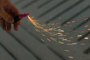 Burning Firecracker with Sparks. Guy Holding a Petard in a Hand. Loud and Dangerous New Year's Entertainment. Hooliganism with Pyrotechnics. Noise of Firecrackers in Public Places photo