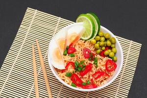 Beautiful Noodle Dish with Green Pea, Eggs, Red Hot Pepper, Greens and Lime with Chopsticks on Sushi Mat. Instant Noodles photo