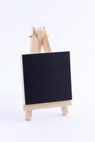 Wooden Easel Miniature with Blank Black Square Canvas for Artists and Painters - Mockup. Mini Wooden Stand with Clean Artboard on White Background, Copy Space photo