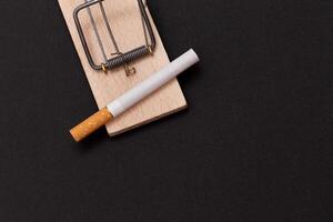 Tobacco Addiction and the World Corporation's Trap - Cigarettes in Wooden Mousetrap on Black Background photo