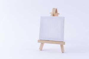 Wooden Easel Miniature with Blank White Square Canvas for Artists and Painters - Mockup. Mini Wooden Stand with Clean Artboard on White Background, Copy Space photo