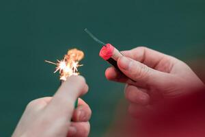 Man Lighting Up Firecracker in his Hand Against the Blue Background Using Gas Lighter photo