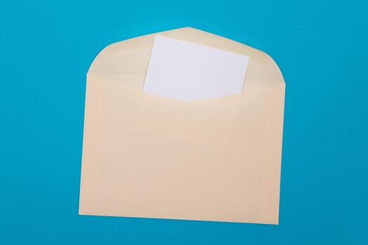 Beige Envelope with Blank White Sheet of Paper Inside, Lying on Blue Background - Mock Up with Copy Space. Receiving Mail or Notice, Sending Postcard - Top View, Flat Lay photo