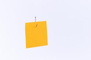 Mockup of a Blank Orange Memo Paper with Copy Space Hanging on a Fishing Hook Against the White Background. Reminder or To Do List. Sticky Note Template photo