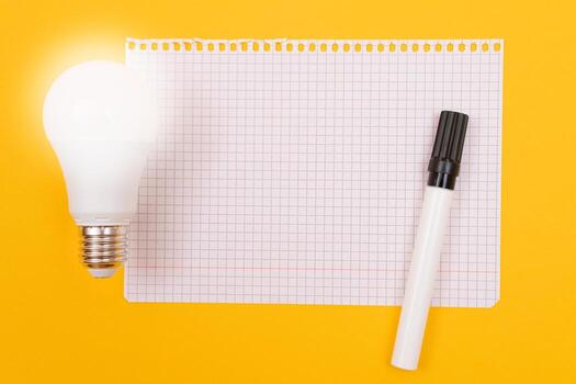 un poder ahorro lámpara con bloc acostado en amarillo mesa, blanco modelo con Copiar espacio - parte superior vista, plano laico foto