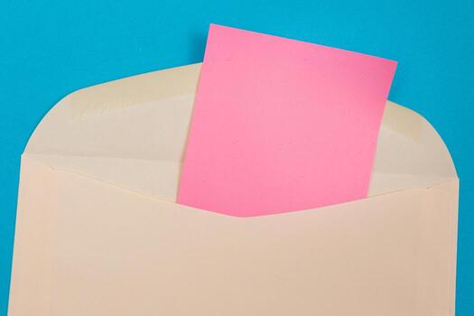 Beige Envelope with Blank Pink Sheet of Paper Inside, Lying on Blue Background - Mock Up with Copy Space. Receiving Mail or Notice, Sending Postcard - Top View, Flat Lay photo