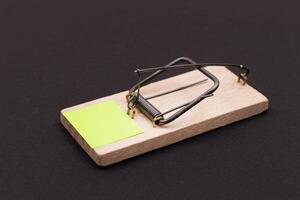 Blank Yellow Sheet of Paper in Wooden Mousetrap - Template. Small Memo Paper in Mouse Trap on Black Background photo