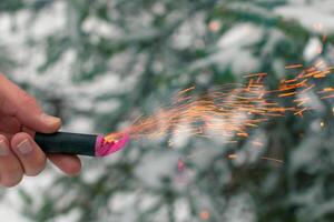 Burning Firecracker in a Hand. Guy Holding a Petard Outdoors in Winter at Daytime. Loud and Dangerous New Year's Entertainment. Hooliganism with Pyrotechnics. Noise of Firecrackers in Public Places photo