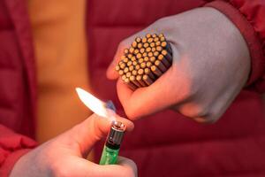 Man in Red Jacked Lighting Up Many Small Black Firecrackers in his Hand Using Gas Lighter. Guy Getting Ready for New Year Fun with Fireworks or Pyrotechnic Products photo