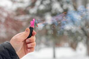 Burning Firecracker in a Hand. Guy Holding a Petard Outdoors in Winter at Daytime. Loud and Dangerous New Year's Entertainment. Hooliganism with Pyrotechnics. Noise of Firecrackers in Public Places photo