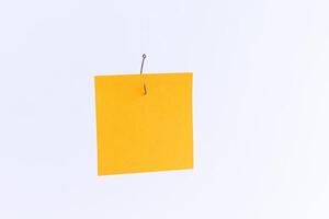 Mockup of a Blank Orange Memo Paper with Copy Space Hanging on a Fishing Hook Against the White Background. Reminder or To Do List. Sticky Note Template photo