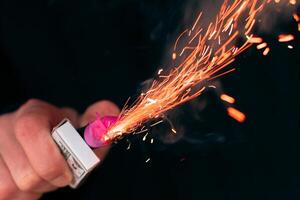 The Firecracker in a Hand. Man Holding a Burning Petard in His Hand. A Human with a Pyrotechnics that Burns with Sparks and Smoke Outdoors photo