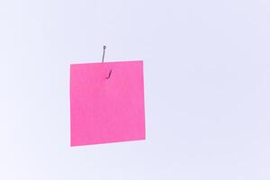 Mockup of a Blank Pink Memo Paper with Copy Space Hanging on a Fishing Hook Against the White Background. Reminder or To Do List. Sticky Note Template photo