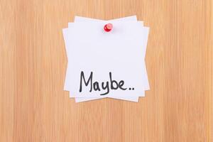 MAYBE.. - White Sticky Notes with Written Word MAYBE, Pinned to the Wooden Message Board. To Do List Reminder in the Office. Memo Note at Work photo