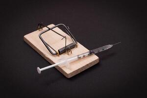Drug Addict, Heroin Hazard or Dose Trap Concept - Disposable Insulin Syringe with Drug Dose Inside Lying in Wooden Mousetrap on Black Background photo
