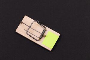Blank Yellow Sheet of Paper in Wooden Mousetrap - Template. Small Memo Paper in Mouse Trap on Black Background photo