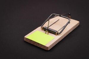 Blank Yellow Sheet of Paper in Wooden Mousetrap - Template. Small Memo Paper in Mouse Trap on Black Background photo