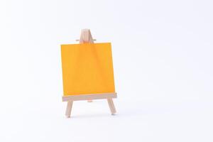Wooden Easel Miniature with Blank Colored Square Canvas or Memo Paper - Mockup. Mini Wooden Stand with Clean Artboard on White Background, Copy Space photo