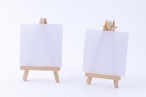 Two Wooden Easels Miniature with Blank White Square Canvas for Artists and Painters - Mockup. Mini Wooden Stand with Clean Artboard on White Background, Copy Space photo