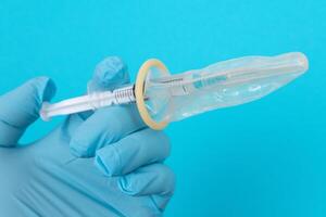 Safe Vaccine, Anti Vaccination Concept - Syringe in a Condom Holds in a Hand with Medical Glove. Mistrust of Vaccination. Natural Immunity. Skepticism About the Vaccine. Freedom and Human Rights photo