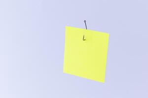 Mockup of a Blank Yellow Memo Paper with Copy Space Hanging on a Fishing Hook Against the White Background. Reminder or To Do List. Sticky Note Template photo